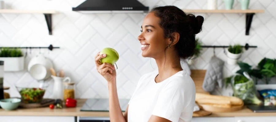 mulher jovem na cozinha de casa comendo ma